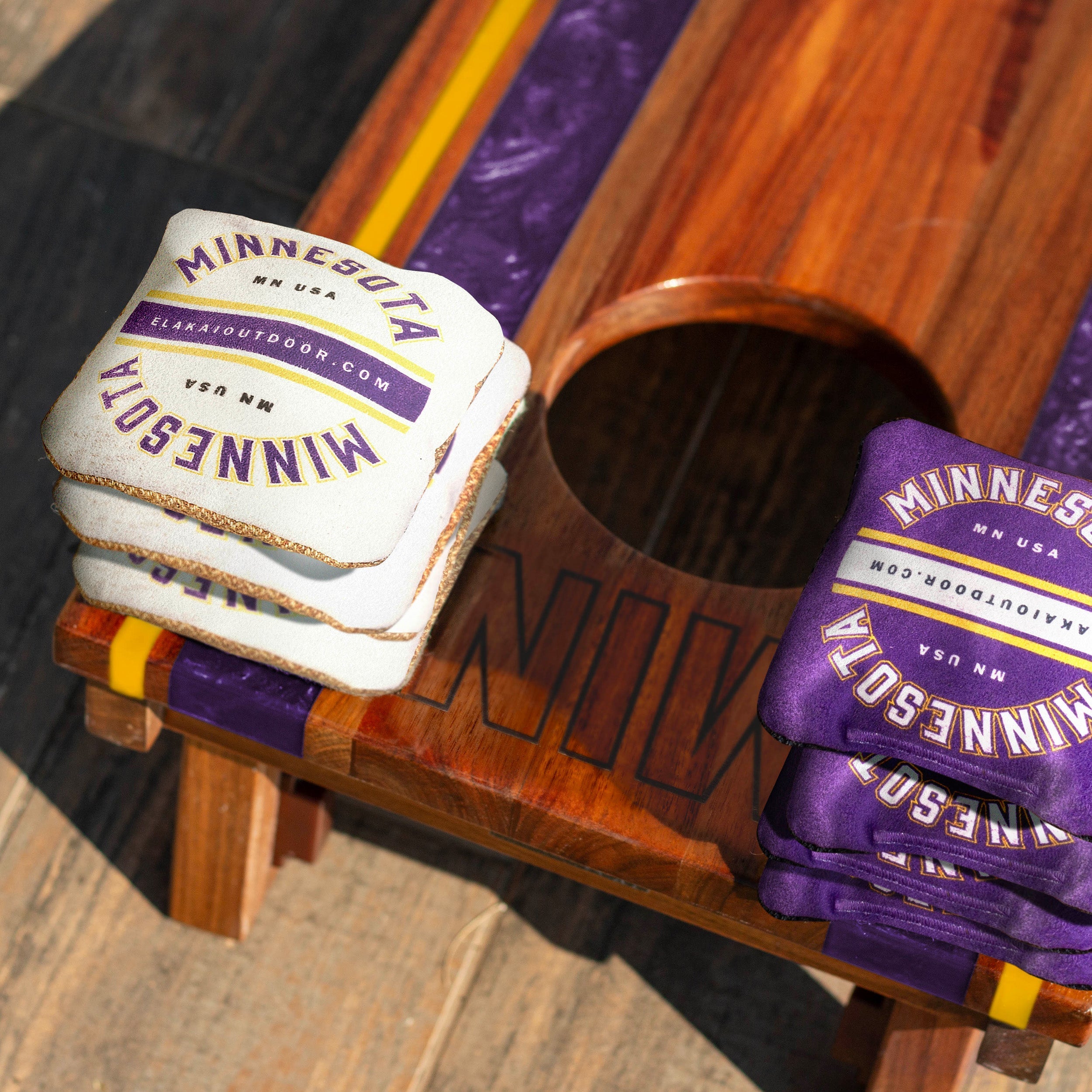 Stack of cornhole bags and purple gloves with 'Minnesota' branding on a wooden surface.

#color_minnesota